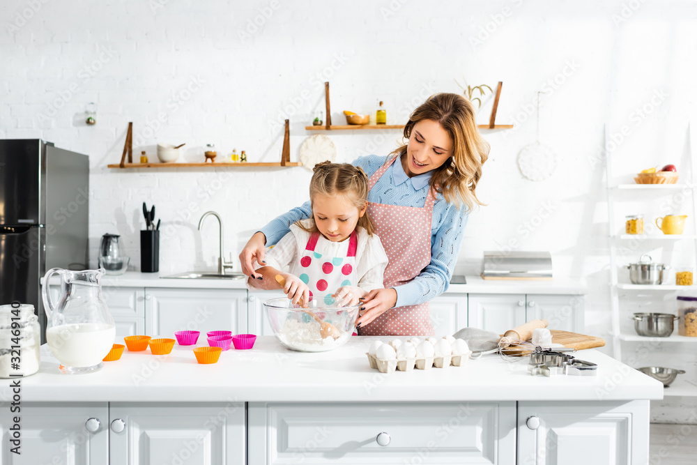 Beautiful attractive mother standing behind cute daughter while kneading dough