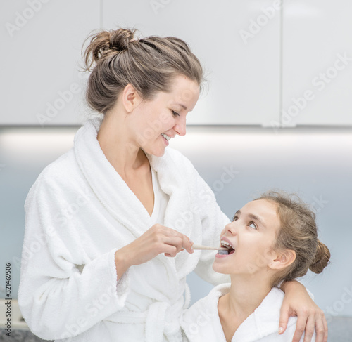 Mom teaching her young daughter how to brush teeth with toothbrush