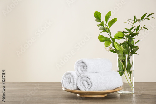 Fresh rolled towels and green branches on grey wooden table