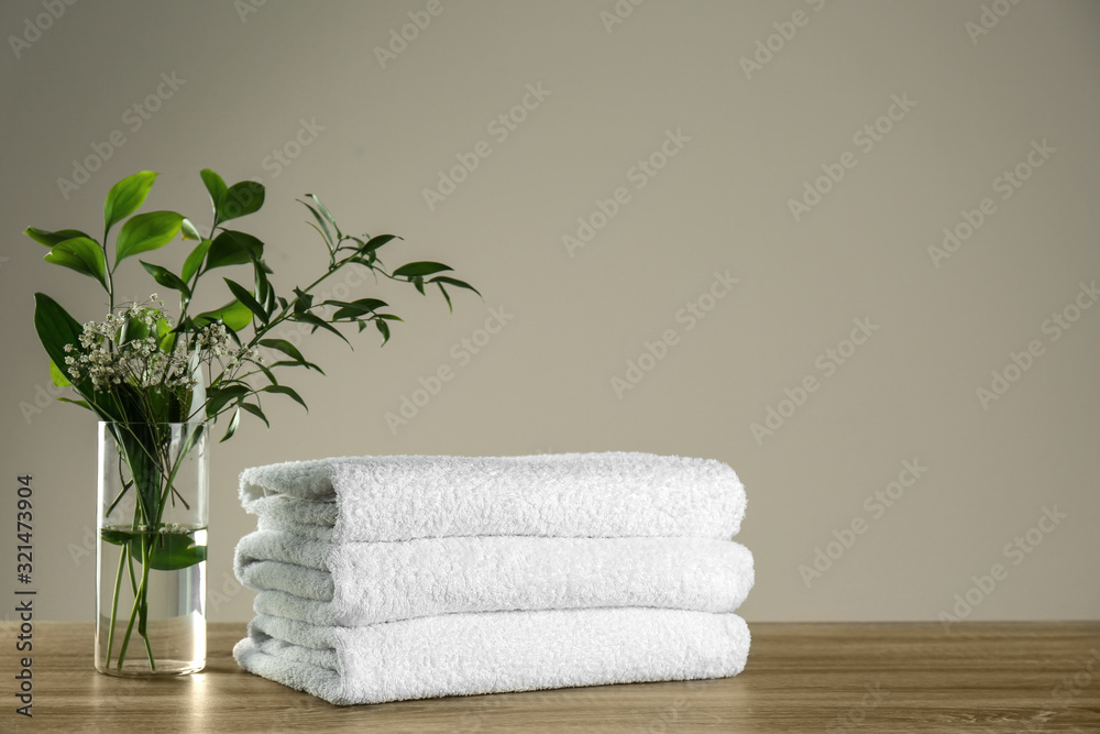 Clean bath towels and vase with green plants on wooden table. Space for text Clean bath towels and vase with green plants on wooden table. Space for text