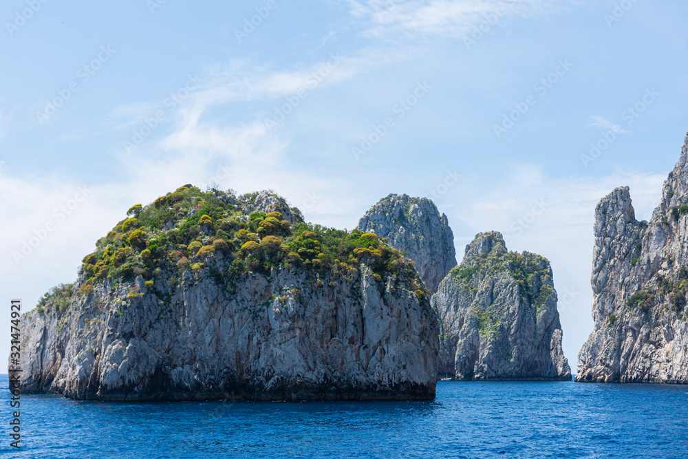 The famous Faraglioni rocks from Capri island, Italy. Sunny summer weather with blue sky and white clouds. The famous Faraglioni rocks from Capri island, Italy. Sunny summer weather with blue sky and white clouds.