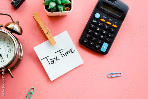 tax time concept on sticky note, calculator and clock on pink background photo