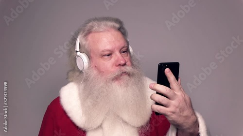 Senior Caucasian smiling man in Santa Claus suit with splendid grey hair, mustache and beard, talking on sell phone with funny expression. Funny portrait of European merry people on white bacground