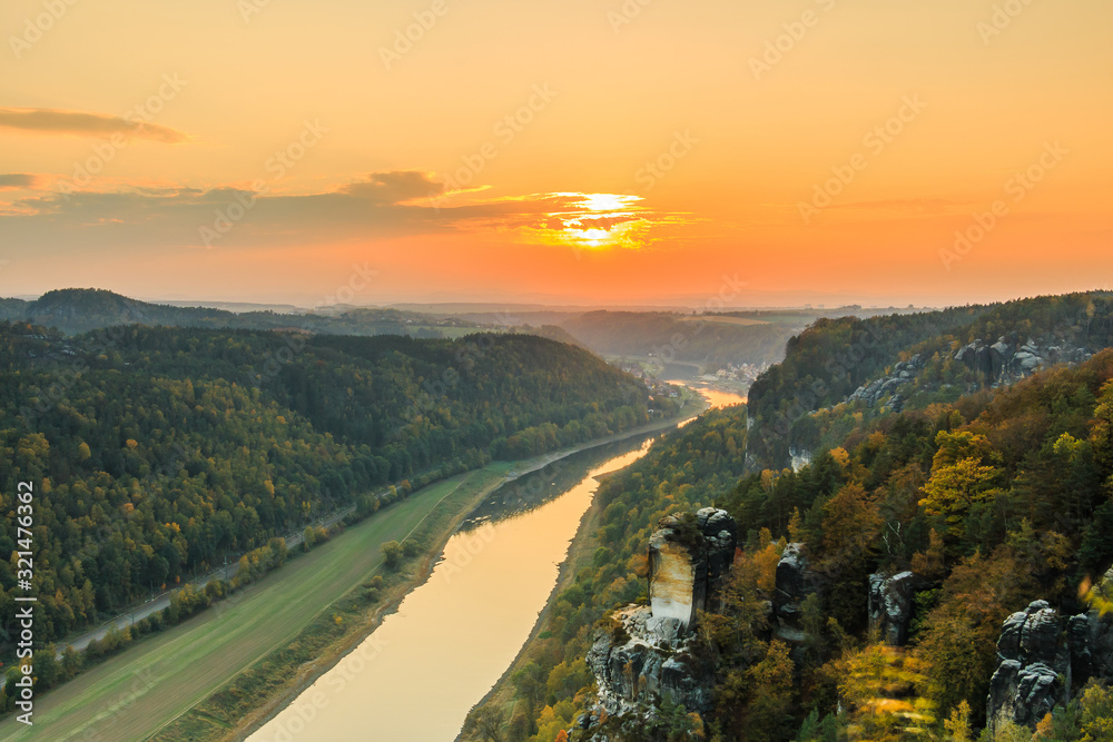 Fototapeta premium Saxon Switzerland National Park with the Elbe Valley.. Landscape with a view from Bastei Bridge with the Elbe and rocks, trees and forests in the autumn mood with an orange horizon at sunset