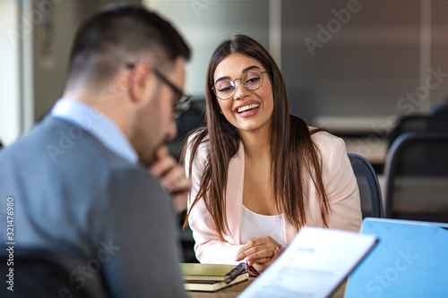 Portrait of young  female client or candidate sitting at table, talking to male manager and smiling in office. Job interview or consultancy concept. Young attractive woman during job interview photo