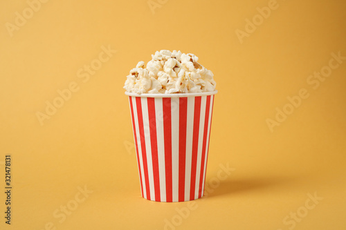 Delicious popcorn in paper cup on yellow background