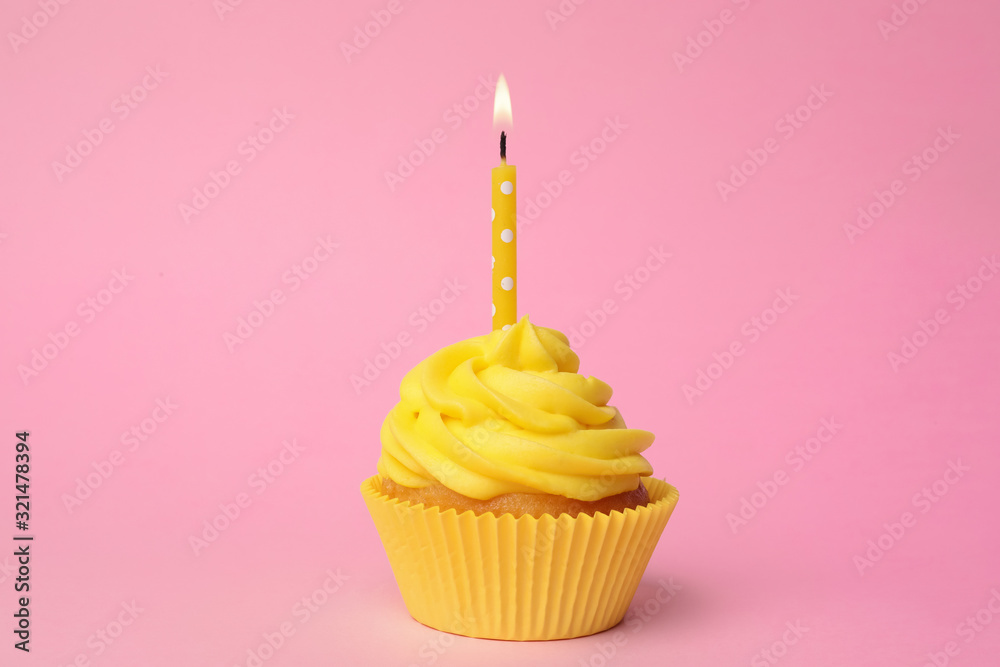 Delicious birthday cupcake with yellow cream and burning candle on pink background Delicious birthday cupcake with yellow cream and burning candle on pink background