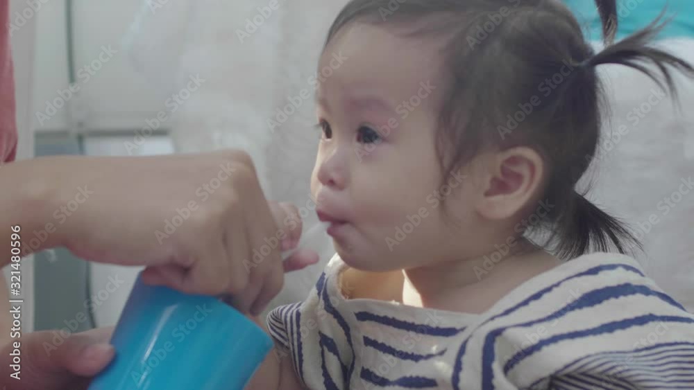 An Asian mother is helping her daughter. To drink from a glass An Asian mother is helping her daughter. To drink from a glass