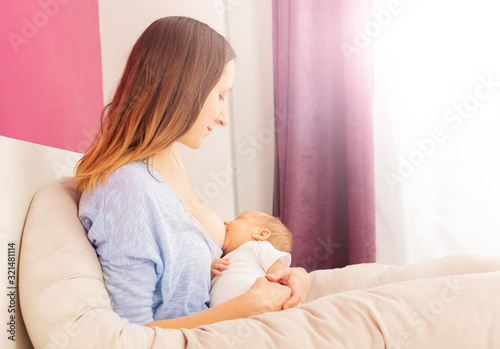 Young mother with long hair breastfeed newborn baby boy sitting in the bed