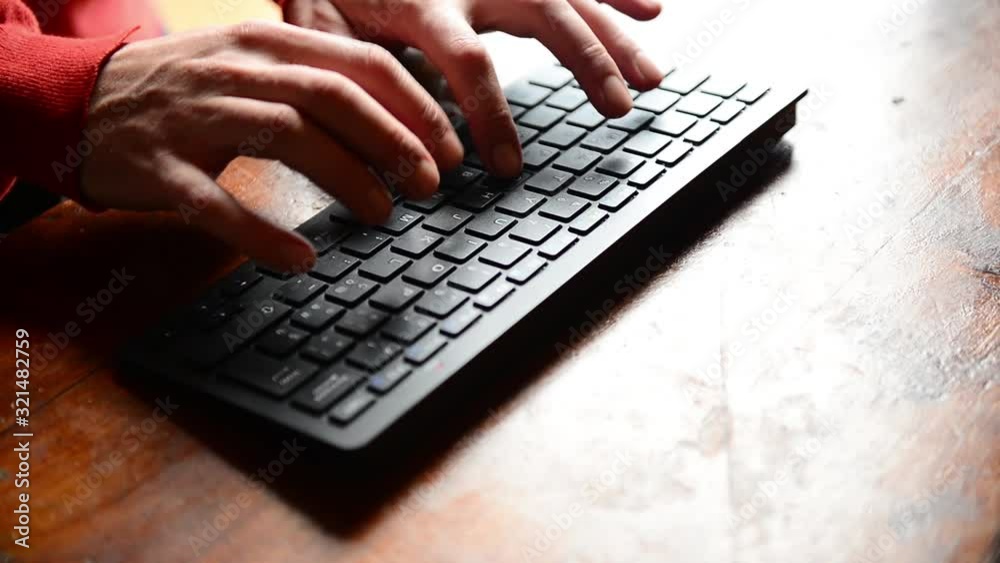 Closeup of caucasian hands typing on black keyword on wooden desk Closeup of caucasian hands typing on black keyword on wooden desk