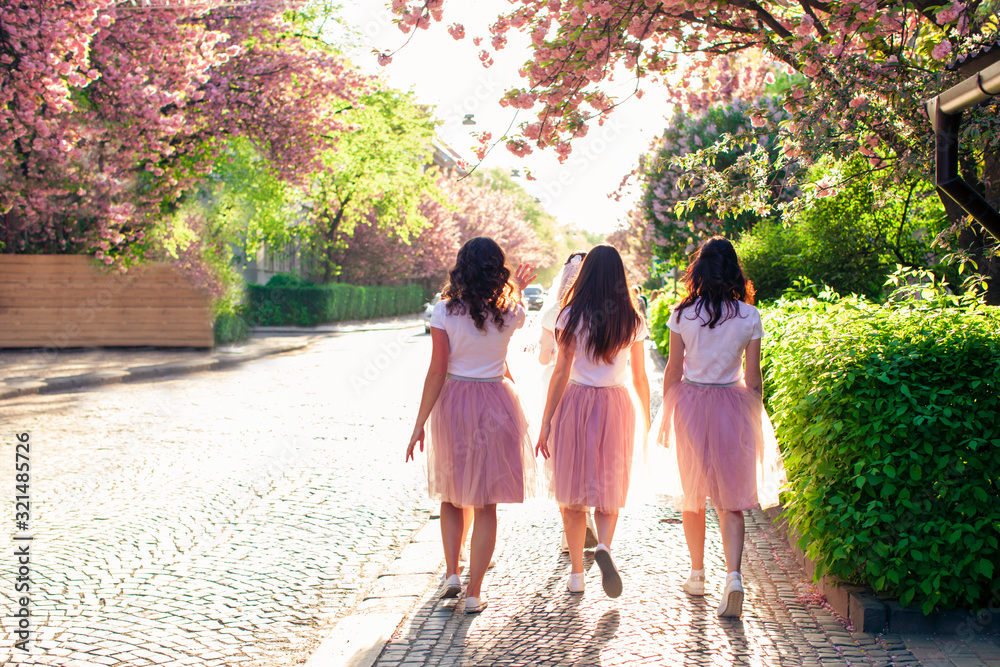 Naklejka premium Group of girlfriends walking city street in springtime while sakura tree is blooming