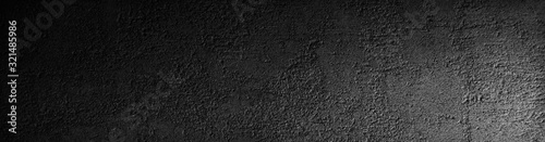 Black grunge background. Rough concrete wall texture in reflection of light closeup. Dark gray grunge banner with copy space for your design.