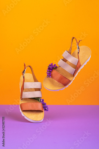 a pair of dancing yellow female leather sandals with purple flowers on a orange lilac background for a banner with a copy space.
