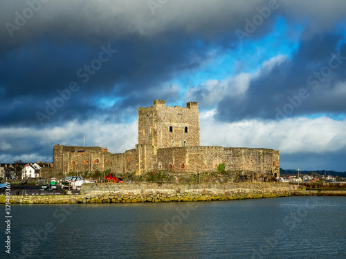 Medieval Norman Castle in Carrickfergus near Belfast, Northern Ireland, with marina in winter. Dramatic sky with dark stormy clouds. Sunset light