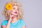 Beautiful blonde girl with voluminous curly hairstyle, in a blue polka dot blouse and with a flower of a sunflower in her hair on a gray background