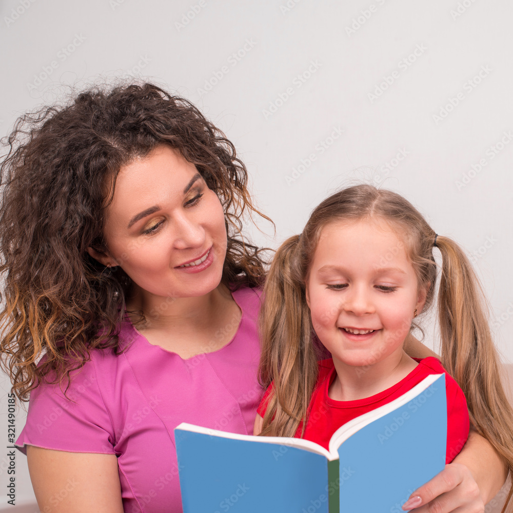 Shot of mother and little daughter spending time together at home. They sit on the couch and read a book. Shot of mother and little daughter spending time together at home. They sit on the couch and read a book.