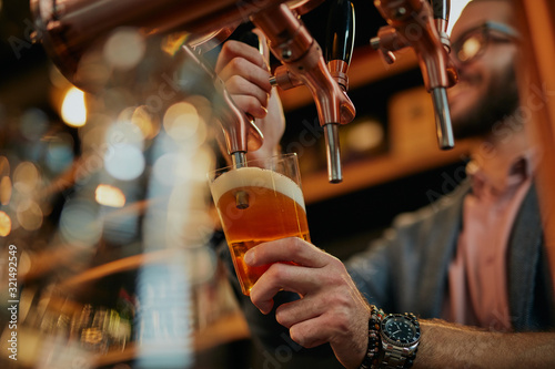 Valokuvatapetti Tattooed caucasian barman pouring beer while standing in pub.