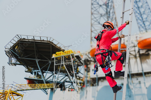 Schilderij op canvas Worker wearing seat belts safety full harness go up the stairs fixed ladder on rig driling and heliport parking lot background during maintenance in shipyard