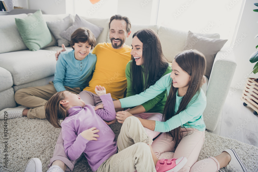 Nice attractive lovely cheerful cheery family three pre-teen kids sitting on floor playing tickling having fun at light white interior style house flat apartment living-room indoors