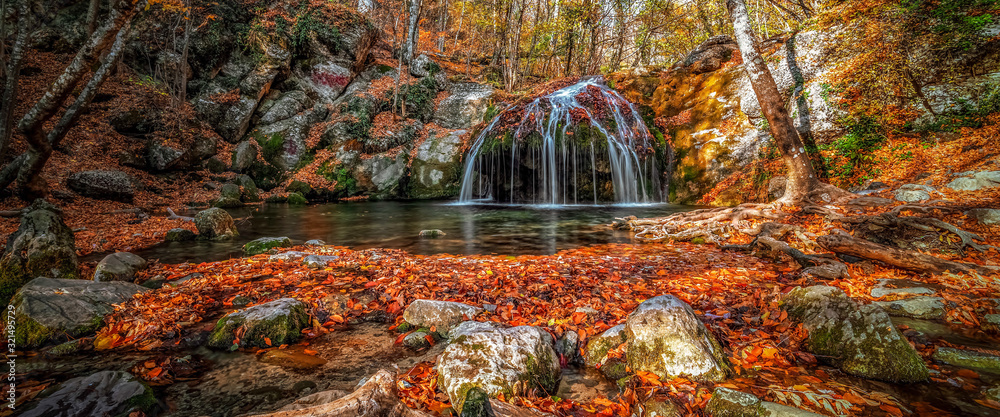 Waterfall in the forest in autumn among the fallen colorful bright leaves. - obrazy, fototapety, plakaty 