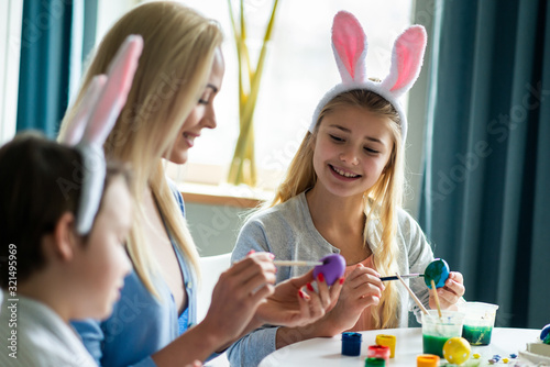 Portrait of happy family are painting eggs during preparing to Easter. They sitting at the table. Focus on girl.