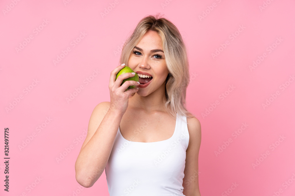 Teenager blonde girl over isolated pink background eating an apple Teenager blonde girl over isolated pink background eating an apple