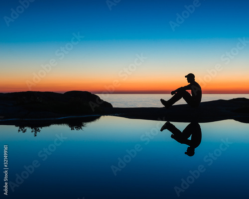Silhouette of a man sitting by a tide pool at sunset. Sweden.