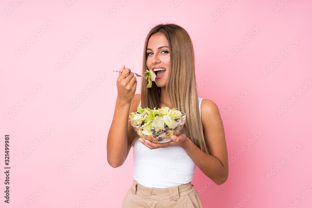 Young blonde woman with salad over isolated background - obrazy, fototapety, plakaty 