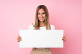 Young blonde woman over isolated pink background holding an empty white placard for insert a concept
