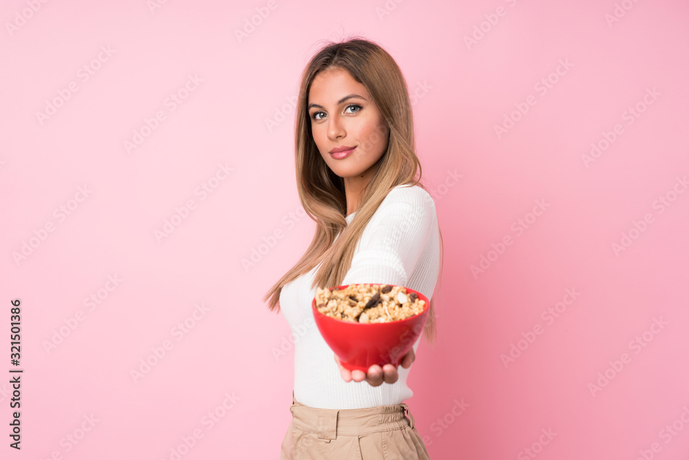 Young blonde woman over isolated pink background holding a bowl of cereals