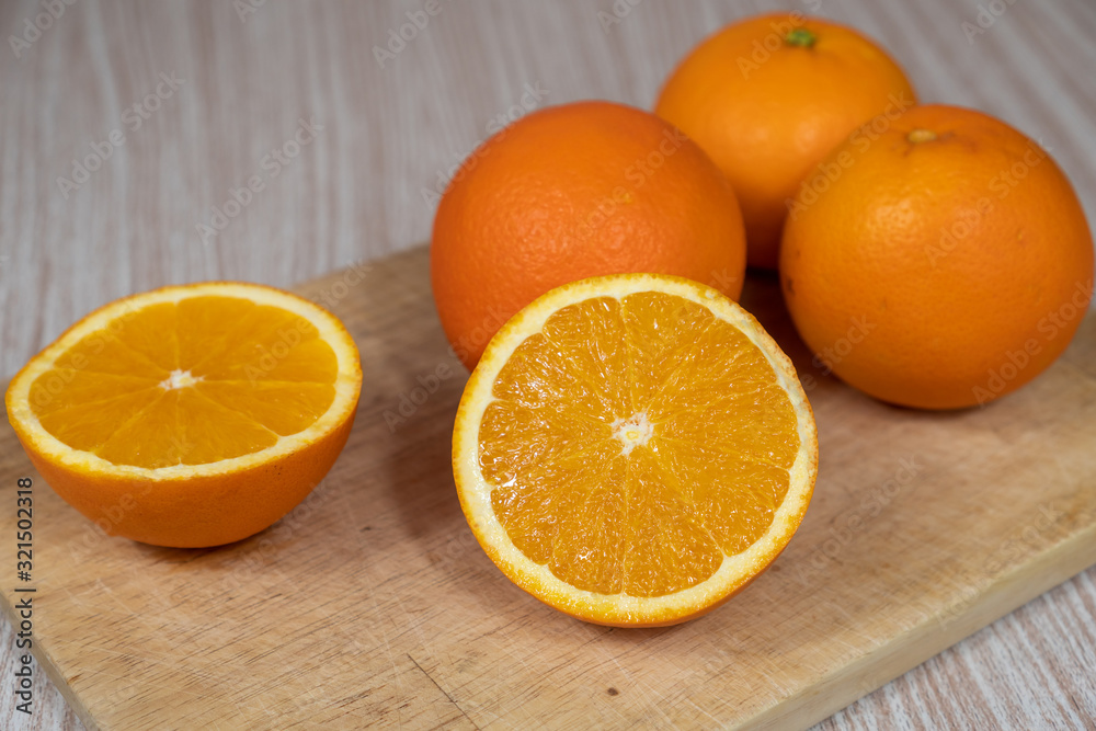Selective focus on a sliced organic orange on a chopping board next to three oranges. Selective focus on a sliced organic orange on a chopping board next to three oranges.