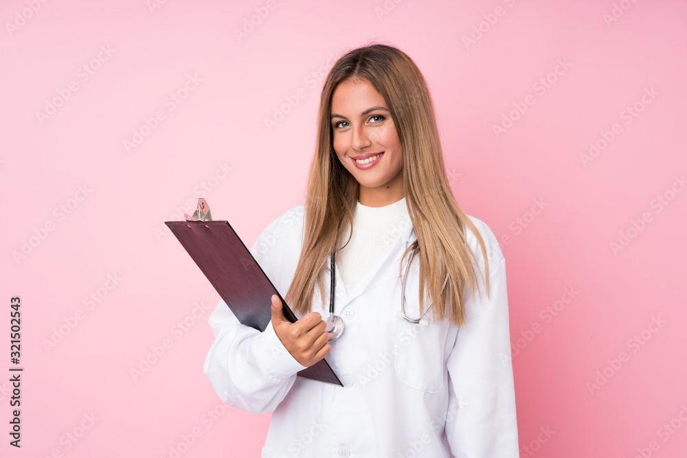 Young blonde woman over isolated pink background with doctor gown and holding a folder Young blonde woman over isolated pink background with doctor gown and holding a folder