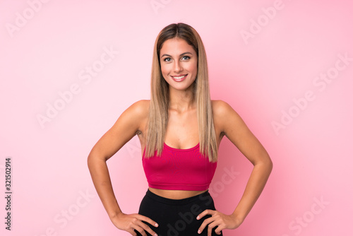 Young sport blonde woman over isolated pink background posing with arms at hip and smiling