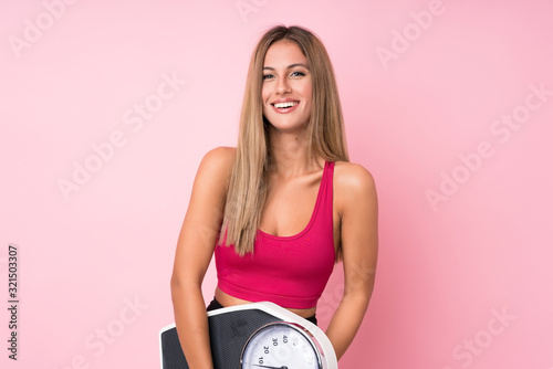 Young sport blonde woman over isolated pink background with weighing machine