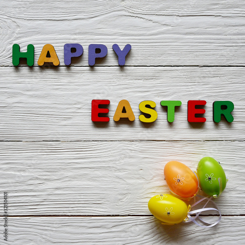 Multi-colored wooden letters making up the words Happy Easter and tree decorative eggs on a white wooden background. Top view. Bright spring Easter background. 
