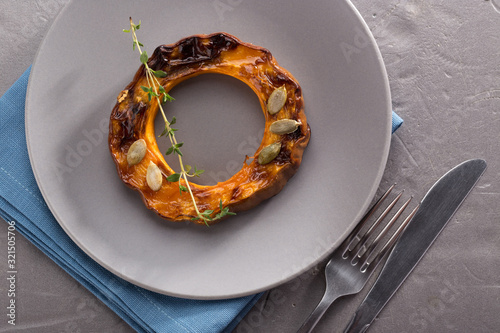 Pumpkin grill served on a plate. Baked pumpkin sliced rings with a knife, fork and napkin on a concrete table. Autumn dish. Halloween dish. Everyday autumn kitchen. Orange colors. space for text.   photo