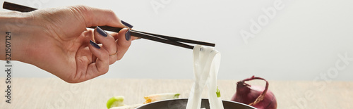 cropped view of woman eating rice noodles isolated on grey, panoramic shot