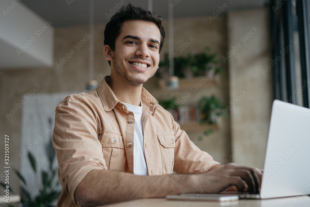 Portrait of happy Indian student studying, learning language. Mixed race business man using laptop computer, typing on keyboard, looking at camera and smiling. Copywriter working freelance project Portrait of happy Indian student studying, learning language. Mixed race business man using laptop computer, typing on keyboard, looking at camera and smiling. Copywriter working freelance project