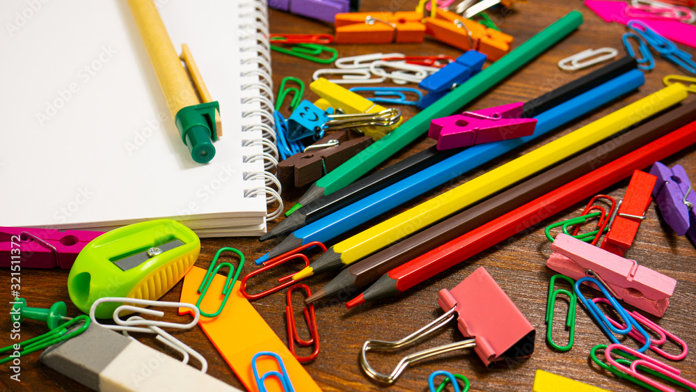 Multicolored Pencils, Paper Clips and Notebook. School stationery on brown wooden table. Back to school, education or knowledge