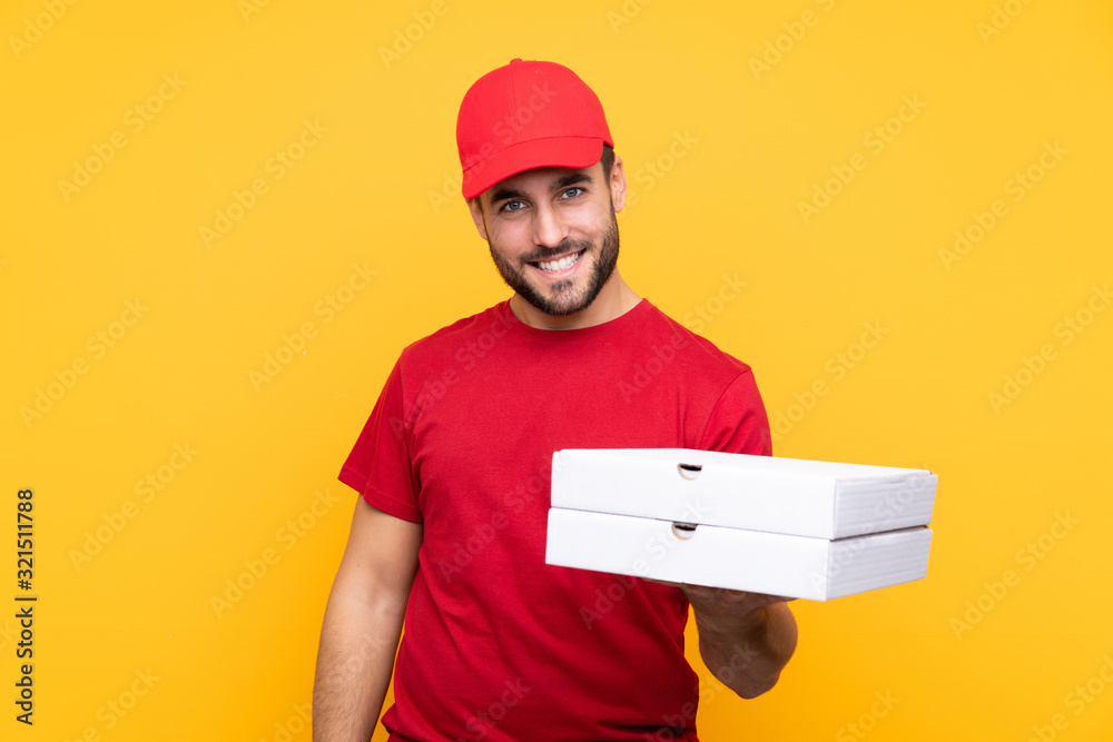 pizza delivery man with work uniform picking up pizza boxes over isolated yellow background with happy expression