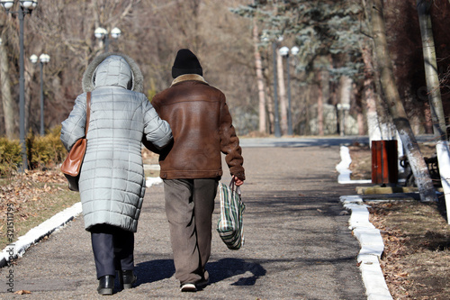 Photos Elderly woman and man with bags walking down the street, rear view