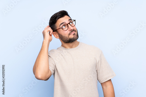 Fotografie Young handsome man with beard over isolated blue background having doubts and wi