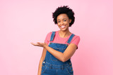 African american woman with overalls over isolated pink background extending hands to the side for inviting to come