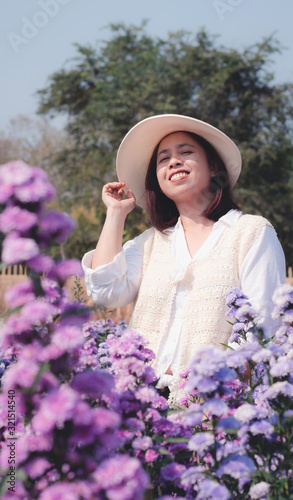 Asian middle-aged women wearing a white sombrero enjoying Purple margaret field, .Relaxing outdoor, Having fun, Holding plant, Happy lady and spring green nature, Selective focus.