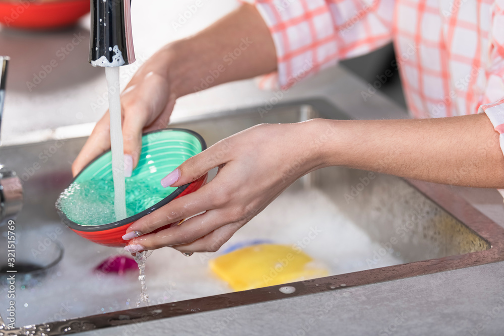 Woman rinsing a bowl under a faucet Woman rinsing a bowl under a faucet