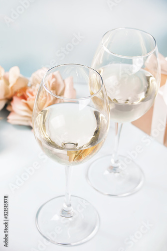 Two glasses with white grape wine with roses and gift box on the background. Romantic dinner concept.
