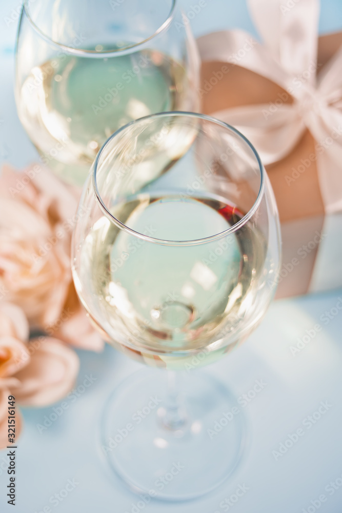 Two glasses with white grape wine with roses and gift box on the background. Romantic dinner concept. Two glasses with white grape wine with roses and gift box on the background. Romantic dinner concept.
