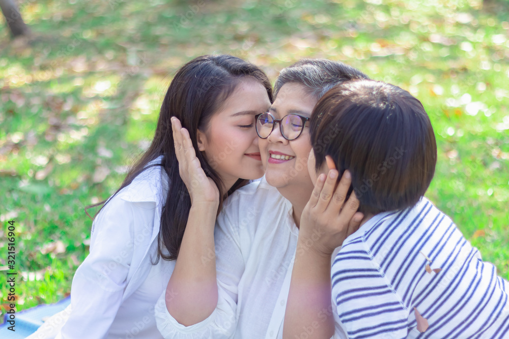Asian lovely young daughter and grandson kiss happy and healthly senior woman or pleasure grandmother in moment of beautiful love in the park. Family generation relationship or bonding photo concept. Asian lovely young daughter and grandson kiss happy and healthly senior woman or pleasure grandmother in moment of beautiful love in the park. Family generation relationship or bonding photo concept.
