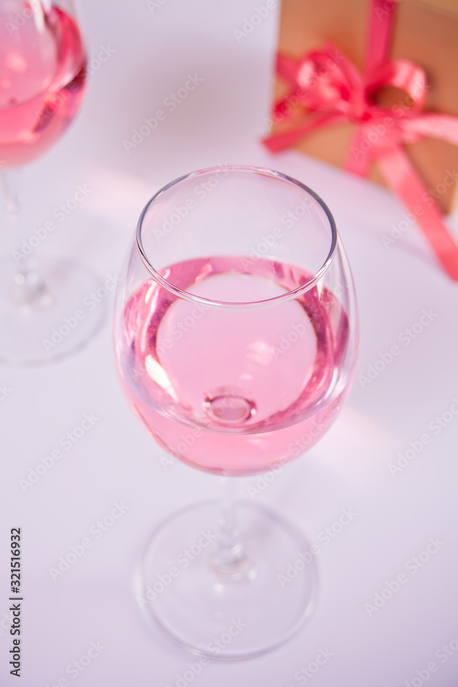 Two glasses with pink grape wine with flowers and gift box on the background. Romantic dinner concept. Two glasses with pink grape wine with flowers and gift box on the background. Romantic dinner concept.