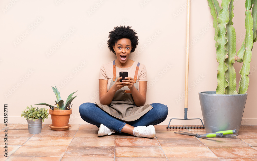 Gardener woman sitting on the floor surprised and sending a message